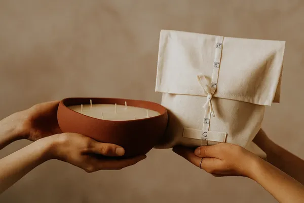 a hand holding a candle and another hand holding a linnen giftbag